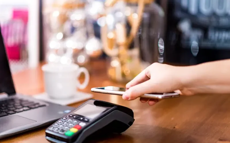 Woman working on laptop, using terminal for contactless payment with smartphone in cafe. Mobile payments Person paying with smartphone for the coffee using POS terminal in cafe. Cashless payment method